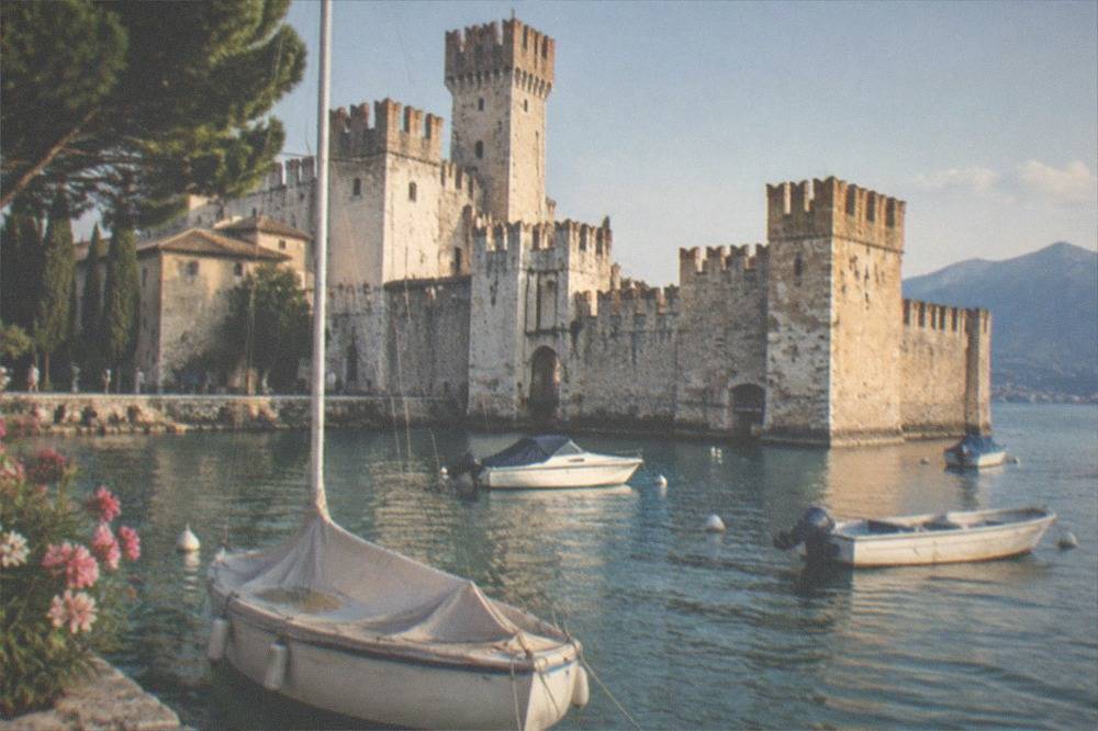 A harbour with small boats moored in front of a medieval castle with crenellated walls