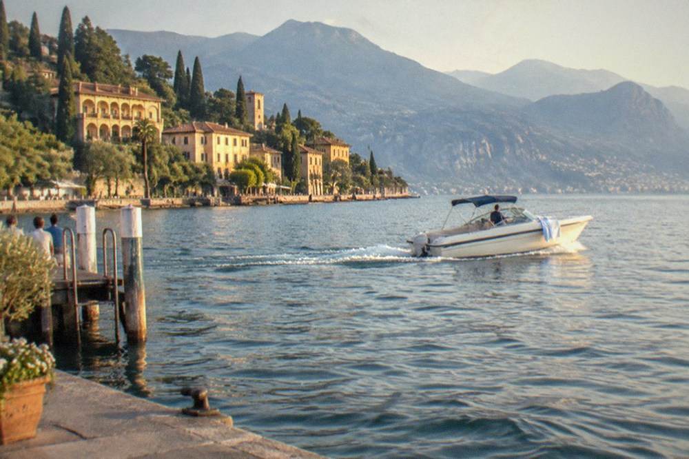 A motorboat crossing open water with a hillside town and distant mountains behind it