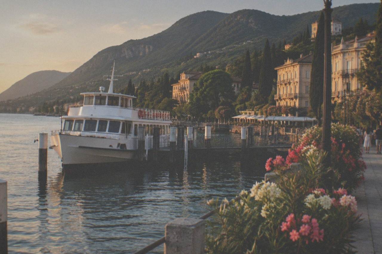 A white passenger ferry moored at a Lake Garda landing stage with hills rising behind the water