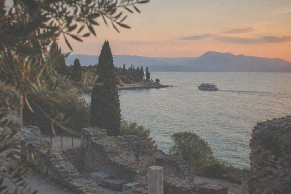 A small passenger boat cruising past the rocky tip of the Sirmione peninsula