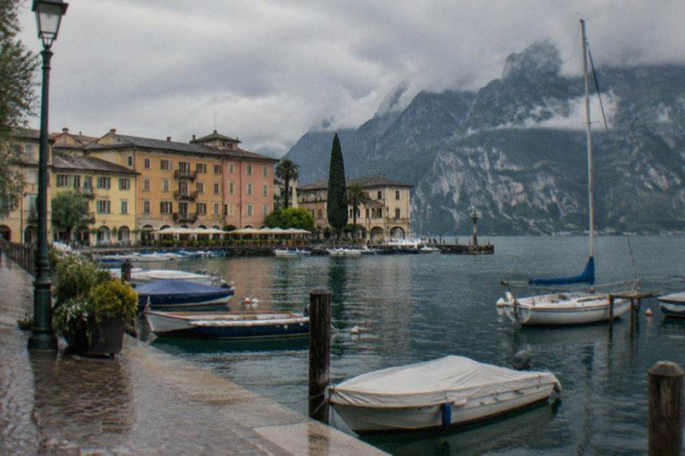 The old harbour of Riva del Garda with pastel buildings along the waterfront and mountains behind.