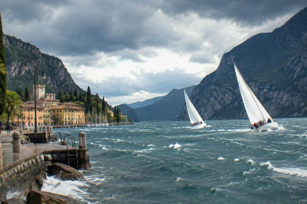 Sailboats heeling in a fresh breeze on the northern basin of Lake Garda with steep mountains on both shores.