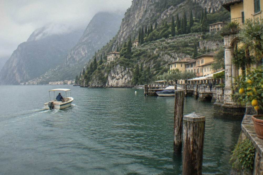A small motorboat cruising past a rocky shoreline with olive trees above the water