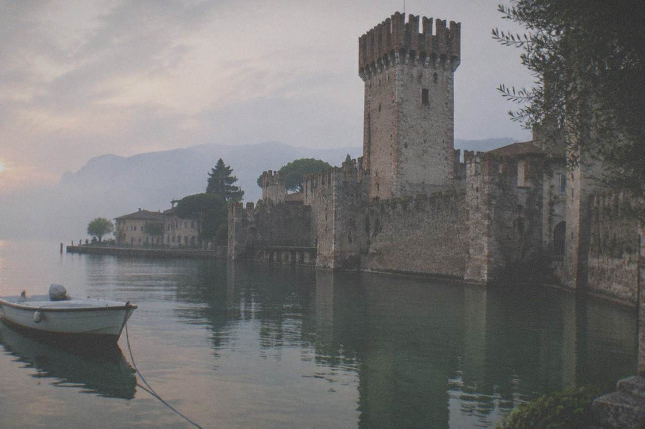 A calm lake with a fortified castle tower rising above a old town at the end of a peninsula