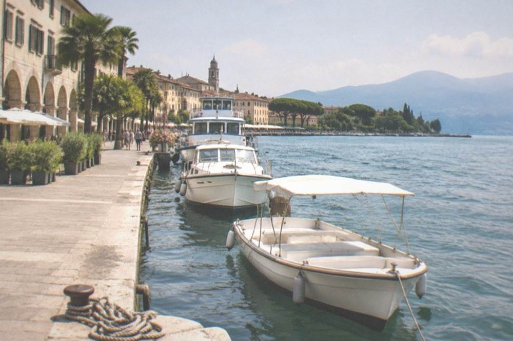 Tour boats of different sizes moored in a row along a sunny lakeside promenade