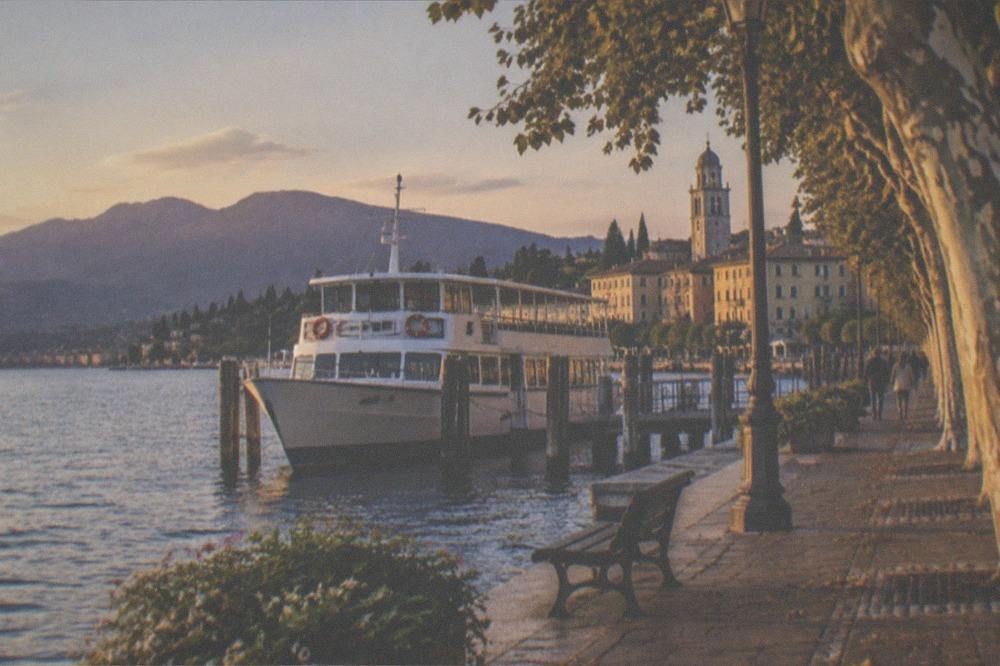 A full-day tour boat at dusk near a lakeside promenade with distant hills