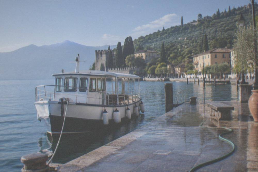 A small cruise boat at a Lake Garda pier in morning light with hills behind