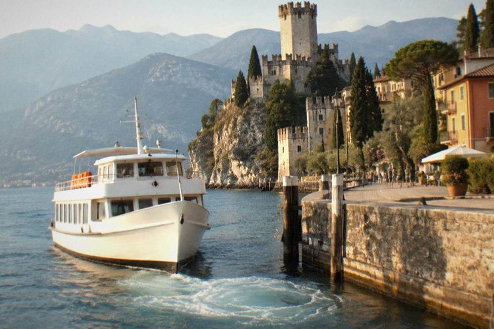 A white passenger boat approaching a stone harbour wall with mountains behind