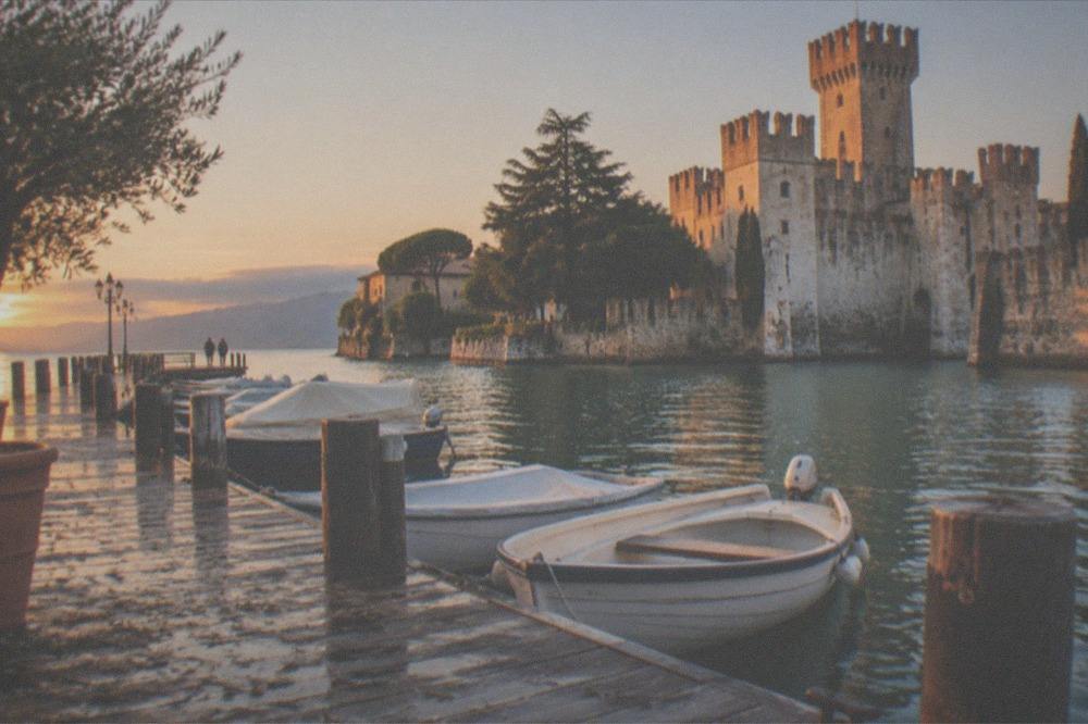 The Sirmione pier at golden hour with boats moored and the castle tower in the background