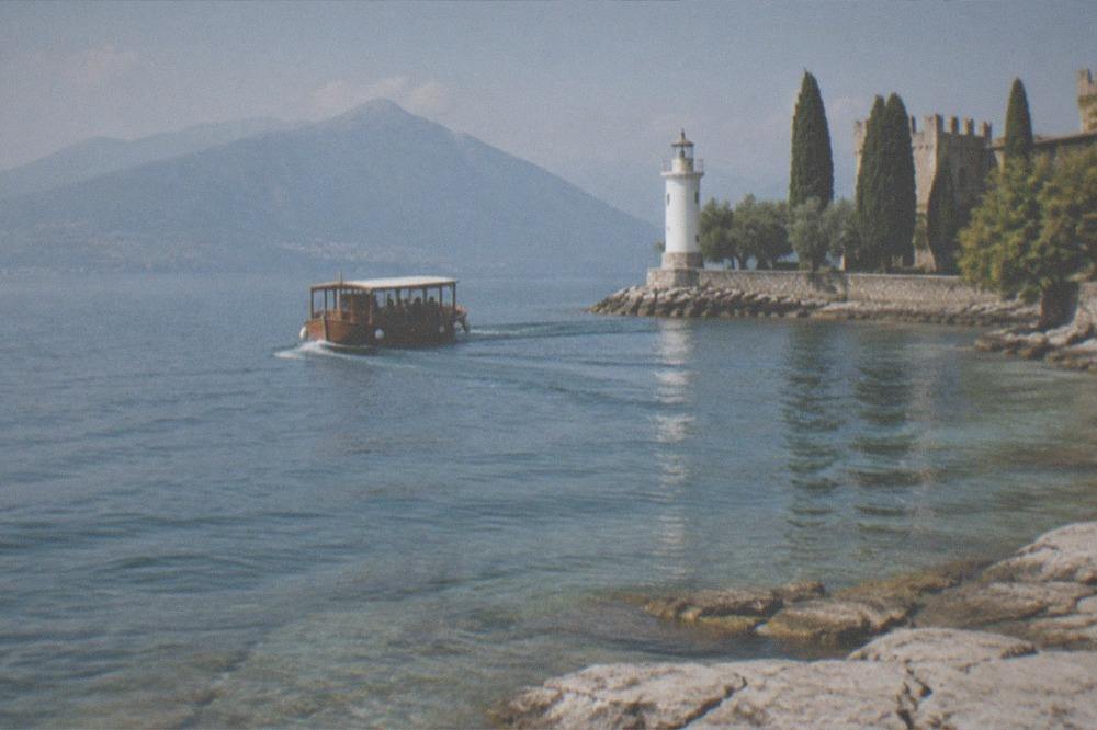 A wooden tour boat rounding a rocky headland with a lighthouse at the tip of a peninsula