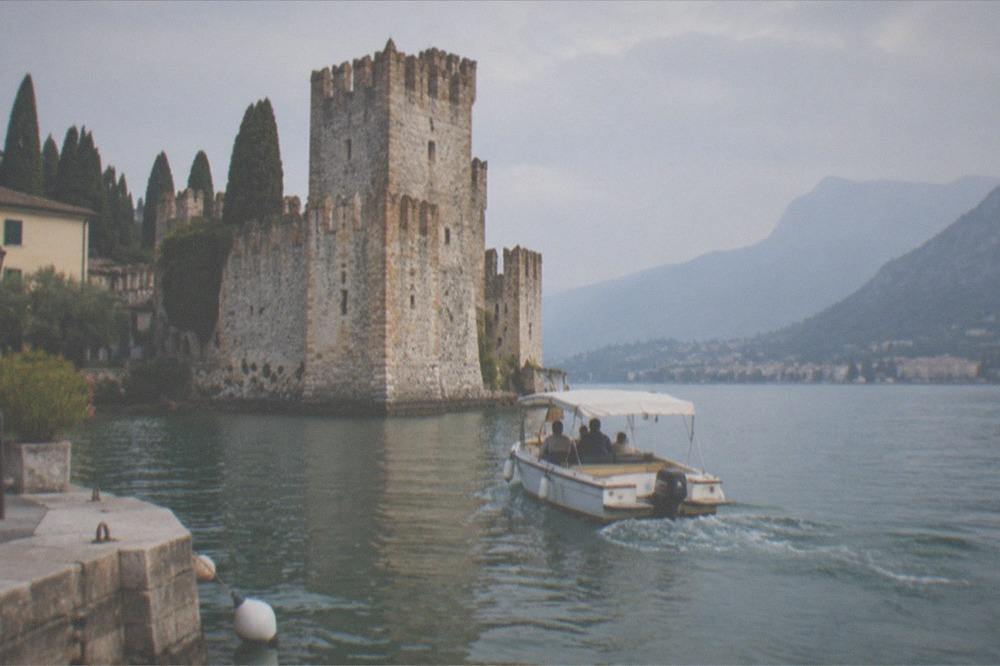 A small boat rounding a rocky peninsula with a historic tower at its tip