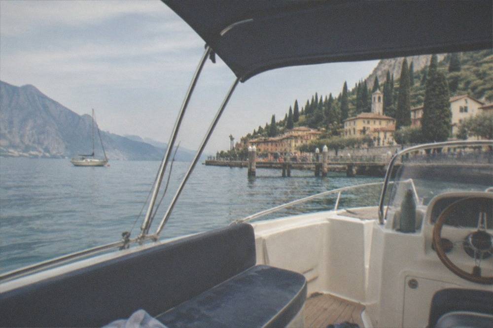 A shaded bimini top on a small private boat on Lake Garda, with calm water and the shore in the distance