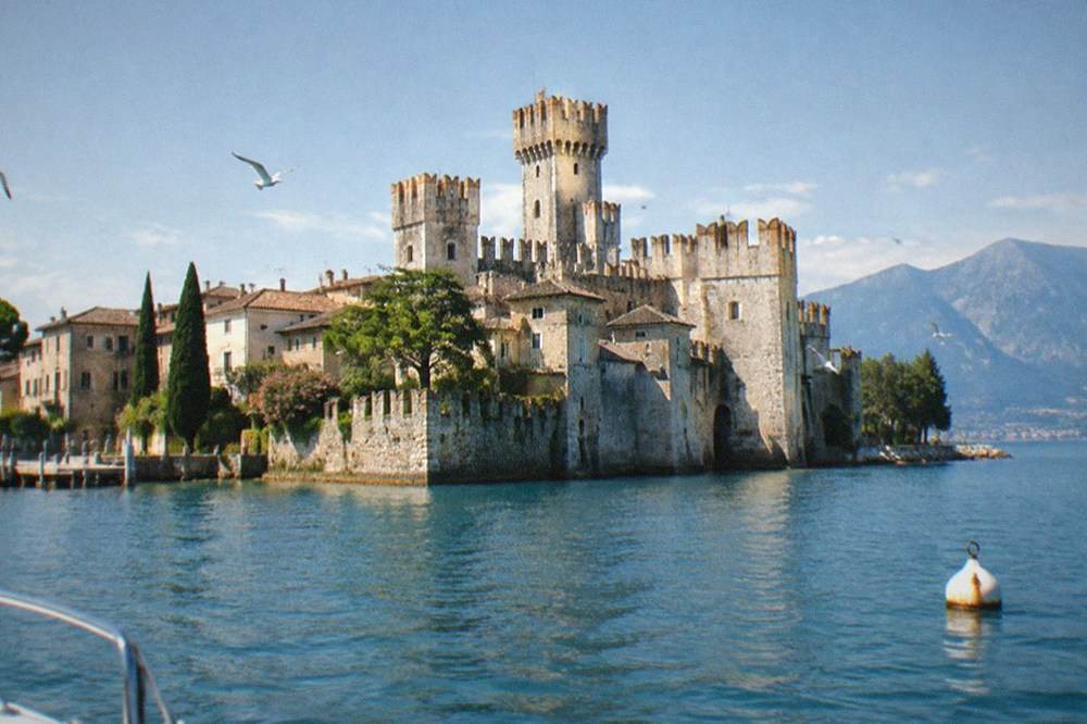 A narrow peninsula with a stone castle rising above rooftops and calm water on both sides