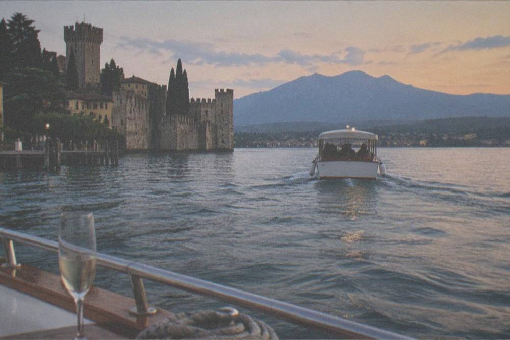A small passenger cruise boat underway on open water toward a distant lakeside village