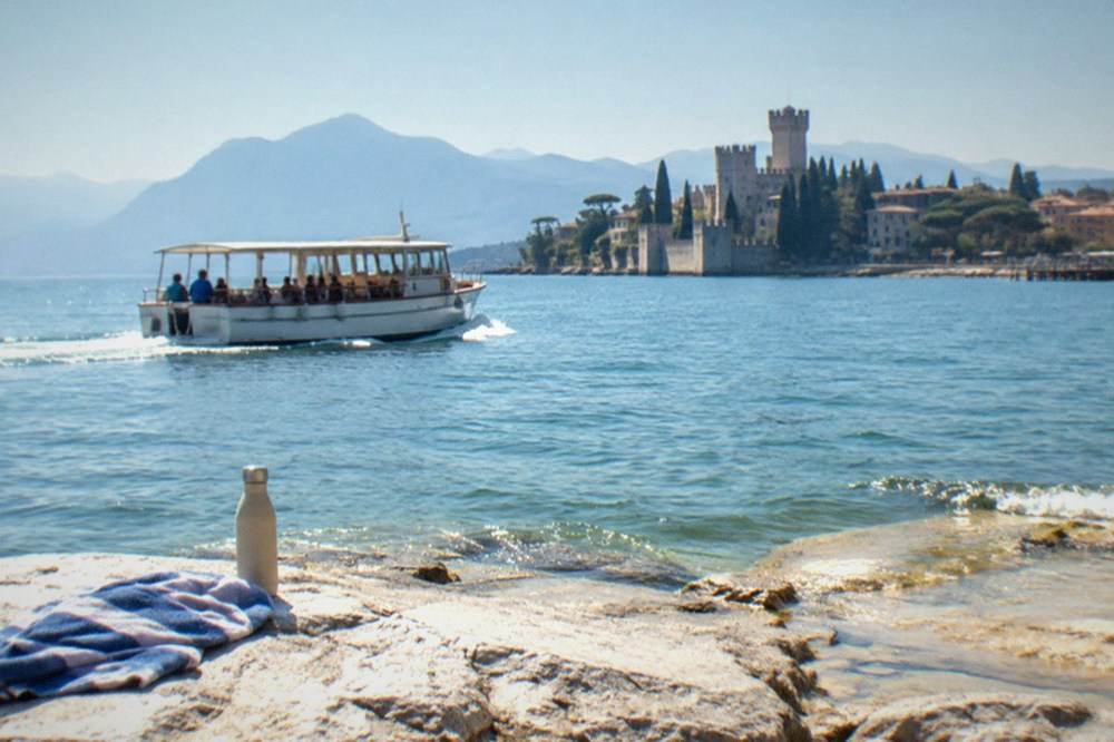 A small tour boat cruising close to a rocky shoreline with a castle in the distance