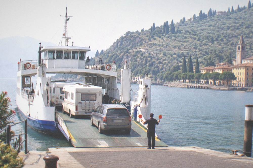 A car ferry loading vehicles at a ramp on the Lake Garda shoreline