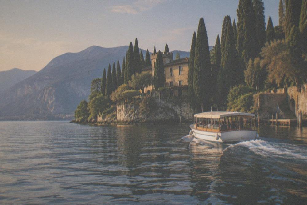 A small tour boat cruising close to a wooded shoreline on Lake Garda