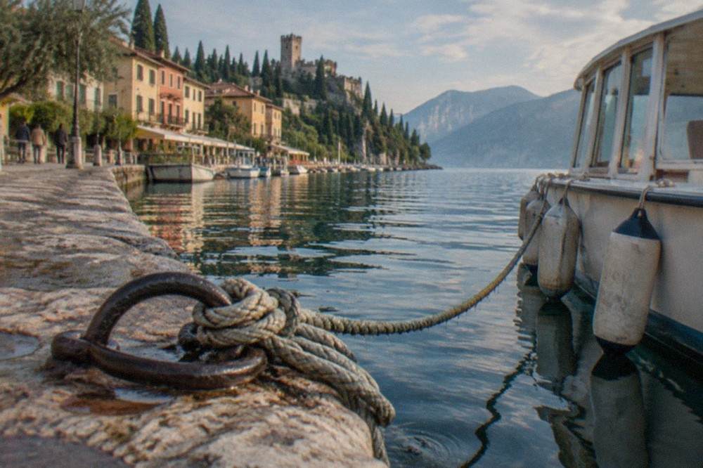 A small passenger boat moored at a Lake Garda pier under soft October light