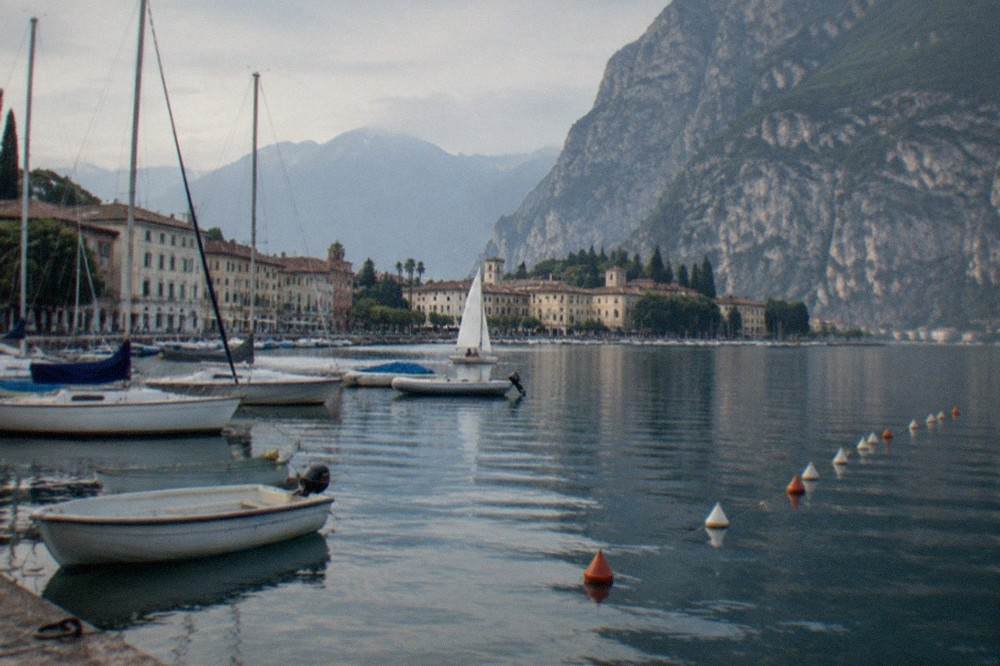 Dinghies and sailboats clustered on the water off a northern Lake Garda town with mountains rising behind