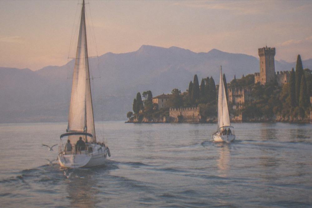 Two sailboats under way on Lake Garda in late afternoon light near a castle town