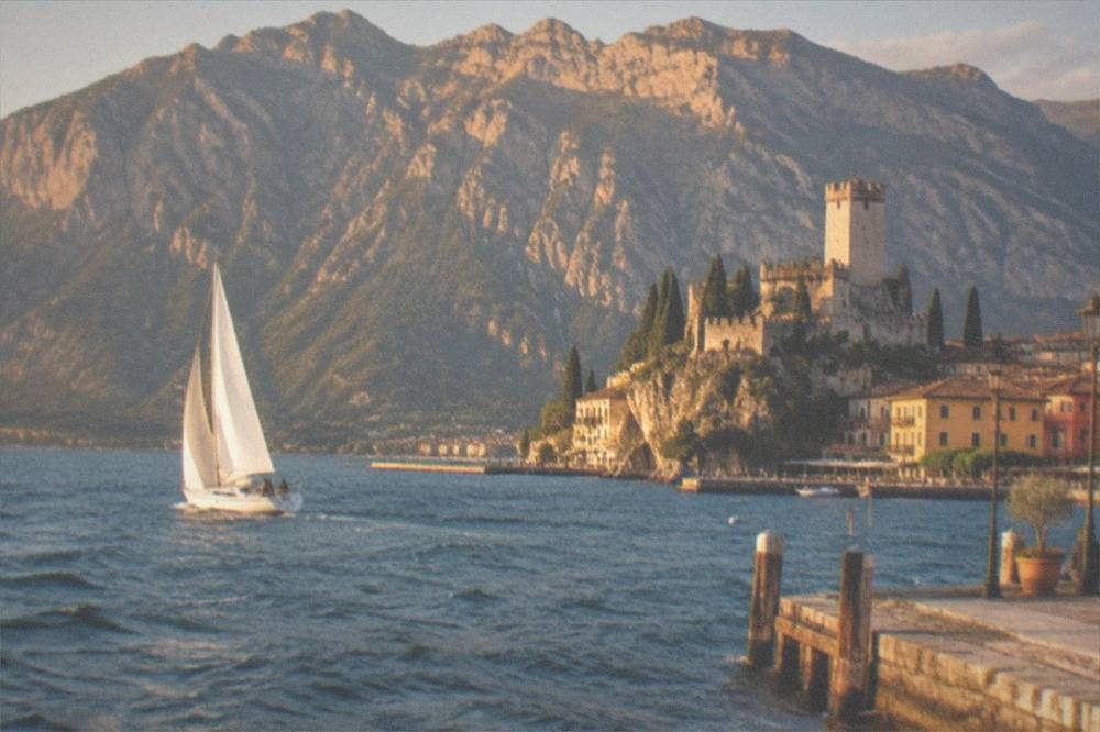 Sailboat on open water beneath the Monte Baldo ridge in late afternoon light