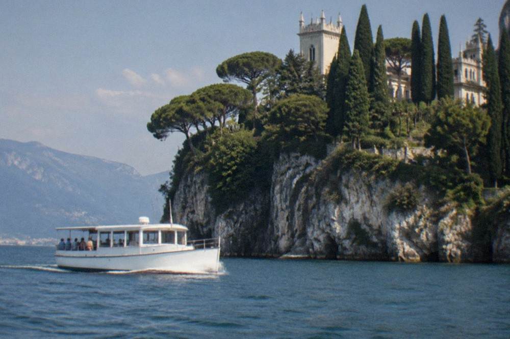 A tour boat passing close to cliffs and cypress trees along a lakeside peninsula