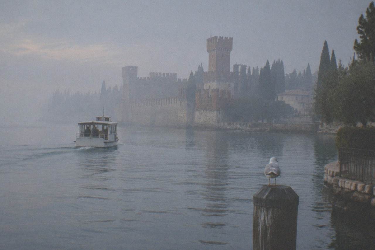 A small boat crossing calm water toward a walled peninsula town on Lake Garda